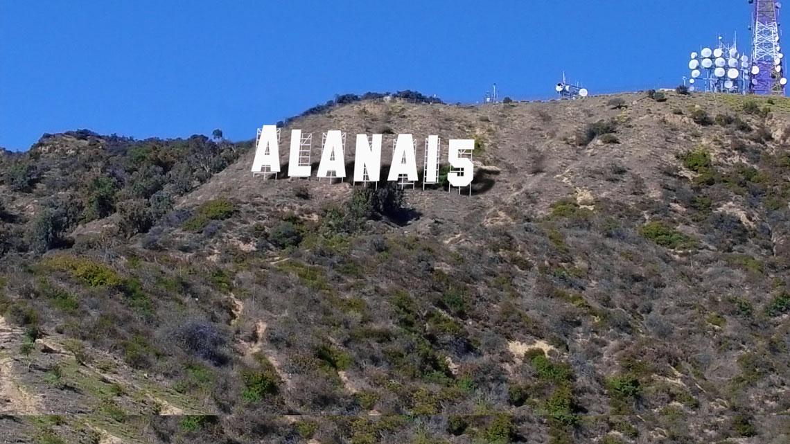 Hollywood-style hillside sign reading “ALANA15” against a clear blue sky.